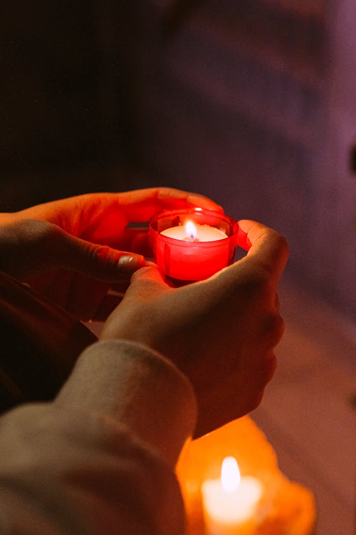 Hands holding a red votive candle flame, symbolizing hope, prayer, and spirituality.